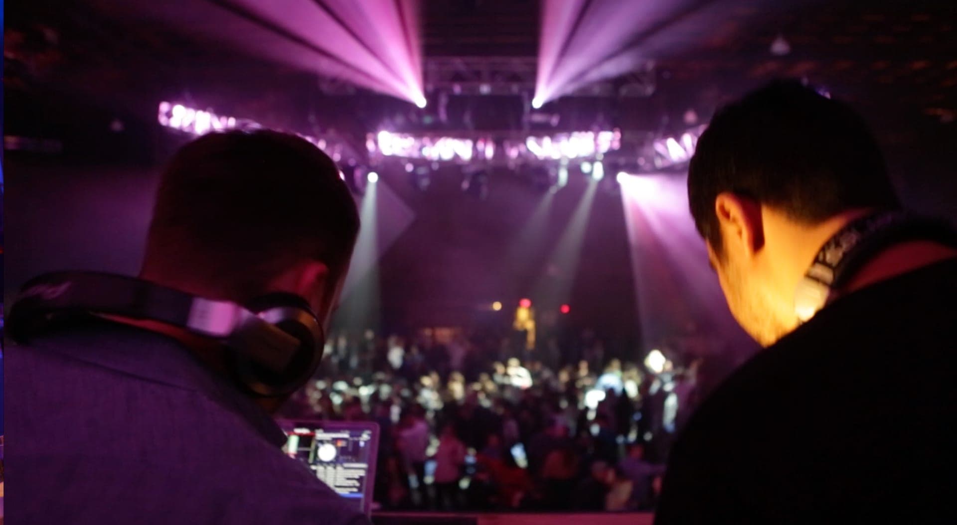 View from behind the DJ booth over a packed dance floor